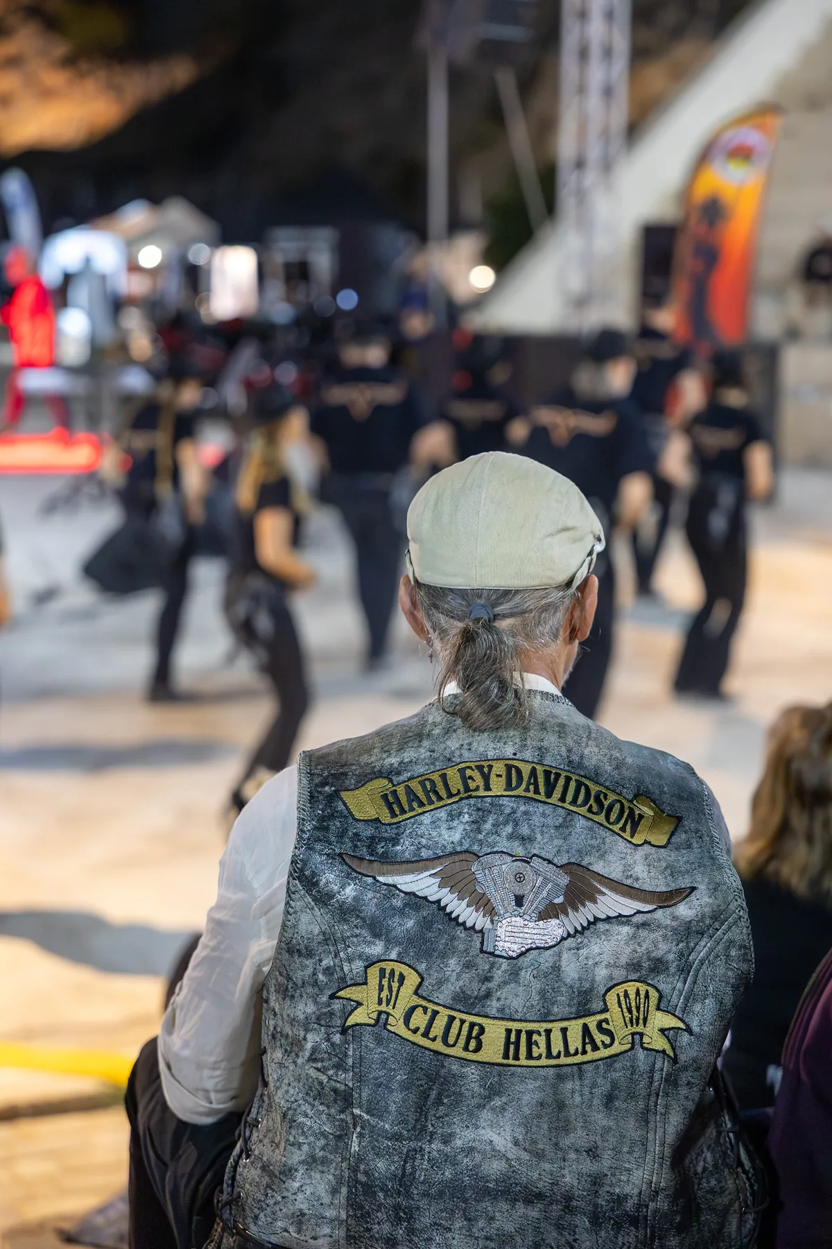 Attendee wearing a Harley-Davidson Club Hellas vest watching the event